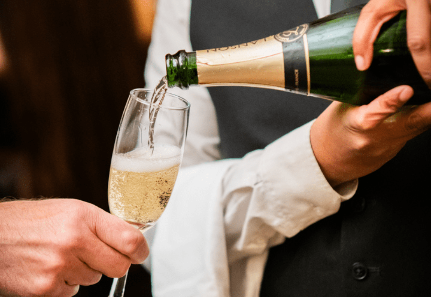 A close-up of a bottle of sparkling wine being poured into a flute held by another person.